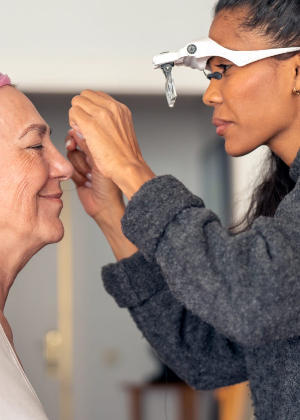 Side view of crop black female cosmetologist plucking eyebrows of client with thread during beauty procedure