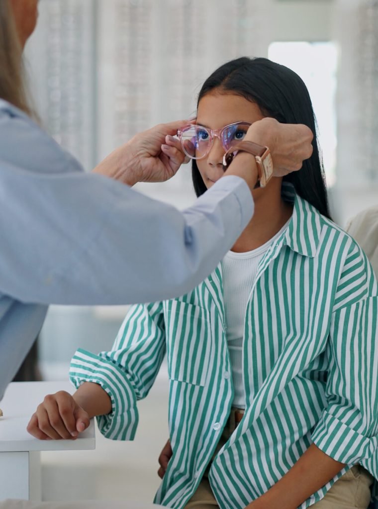 Mother, child and glasses with optometrist for sight, vision or eye care at retail, shop or store. Mom, daughter and mature optician helping customer try on spectacles for size, decision or choice.